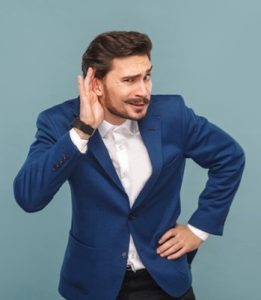 Individual with blue blazer cupping ear with silly look on his face